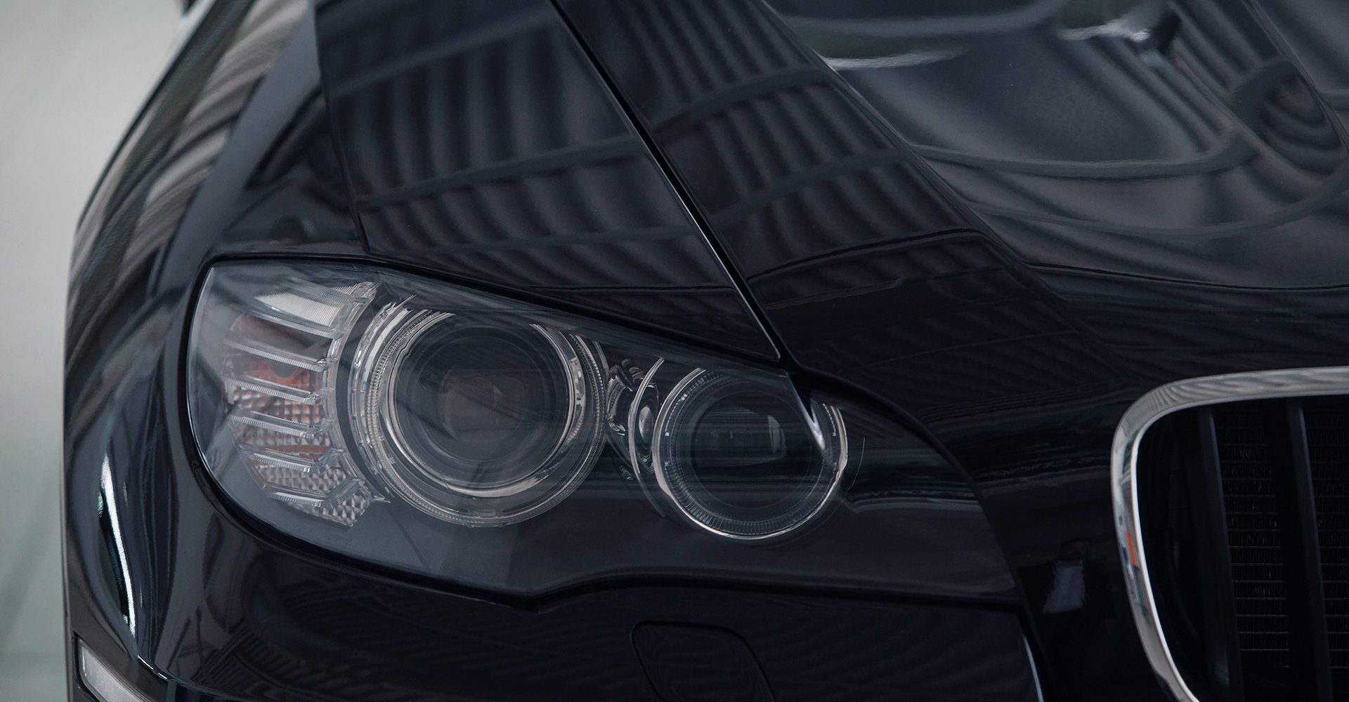 Close-up of a black car's headlight and hood, showcasing sleek design and polished surface, representing Mr.Shine's professional car wash services.