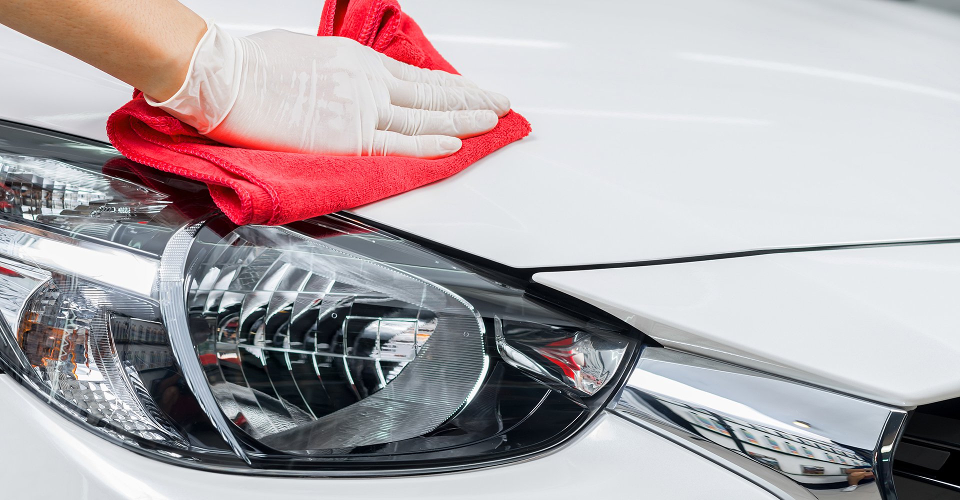 Hand applying premium wax with a red microfiber cloth on a shiny white car hood, highlighting detailing service at Mr.Shine car wash.
