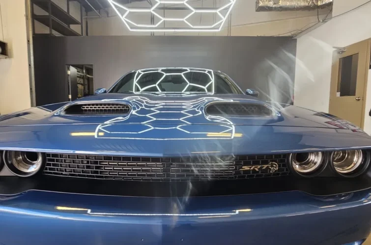 Blue sports car with prominent hood vents and sleek design, showcasing expert detailing and shine, set against a modern garage backdrop with geometric lighting, highlighting Mr. Shine's car wash services in Pickering.